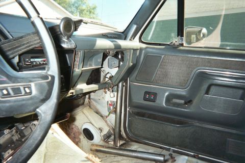 1990 Ford Bronco - Stripped truck cab interior with steering wheel, gray dash and door panel, and a vertical metal tube running through the floor.