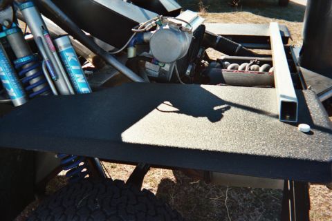 1990 Ford Bronco - Close-up of a tube-framed off-road vehicle's flat black deck flanked by blue King reservoir coilover shocks.