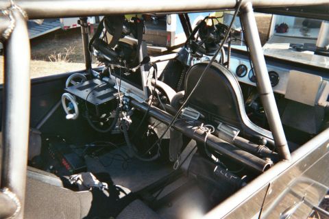 1990 Ford Bronco - Cockpit of a tube-framed vehicle showing twin black racing seats, roll bars and a cluttered dash area.