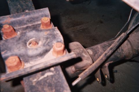 1990 Ford Bronco - Close-up of a worn bolted steel mounting bracket and driveshaft component coated in grease underneath a vehicle.