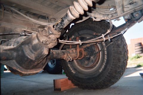 1990 Ford Bronco - Underside view of a truck rear differential, leaf-spring suspension, driveshaft and a BFGoodrich mud-terrain tire raised off the ground.