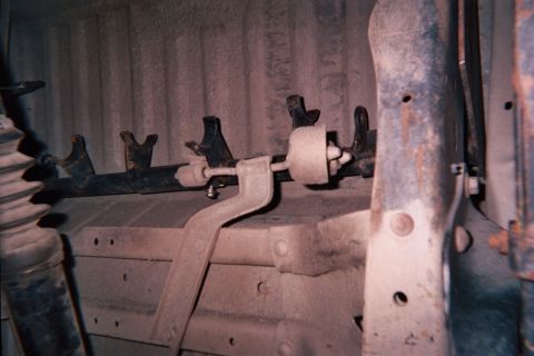 1990 Ford Bronco - Underbody view of a vehicle rear suspension and axle with multiple brackets, sway-bar links and a CV boot against a light-colored backgroun…