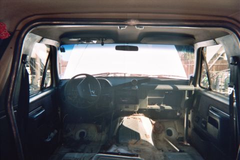 1990 Ford Bronco - Interior of a gutted truck-based SUV showing the dashboard, steering wheel and bare floor with carpet removed.