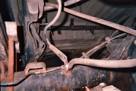 1990 Ford Bronco - Looking up at a vehicle's underbody showing floor pan, crossmember, fuel lines and a draped hose.