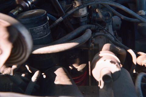 1990 Ford Bronco - Tight engine-bay view showing an oil filter, vacuum hoses, a conical air filter and assorted engine components.