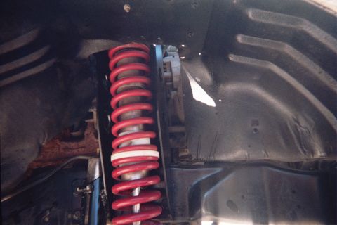 1990 Ford Bronco - red coil spring with white tip seated in a black-painted wheel well next to suspension mounting points.