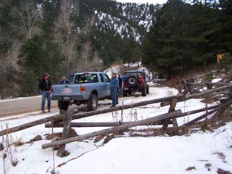 1985 Ford Bronco - A group of people stand around a light blue pickup truck and a red Jeep on a snowy road in a wooded area.