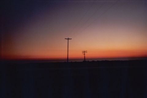 1990 Ford Bronco - Two utility poles and wires silhouetted on the horizon under a gradient orange-to-blue twilight sky.