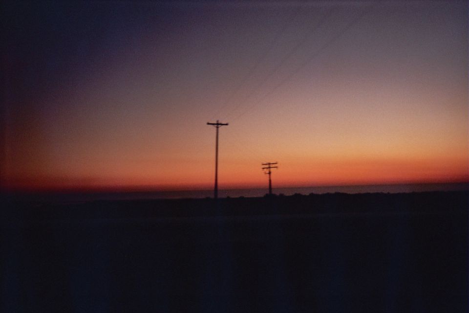 Silhouetted power line poles against an orange and blue dusk sky
