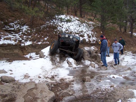 1985 Ford Bronco - An off-road vehicle navigates a challenging snowy and icy trail with onlookers.