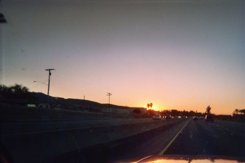 1990 Ford Bronco - Dusk drive on an open multi-lane highway with the sun setting low over distant hills and roadside power lines.