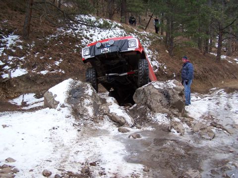 1985 Ford Bronco - Off-road vehicle attempts to navigate difficult terrain with rocks and snow.