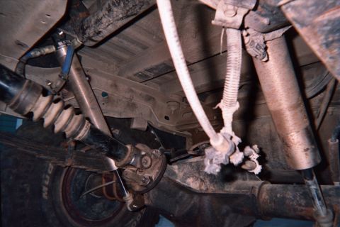 1990 Ford Bronco - Close underbody shot of a truck's drivetrain showing the driveshaft, front differential and a blue-painted suspension arm.