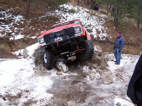 1985 Ford Bronco - Off-road vehicle attempts to climb over rocks and snow-covered ground.
