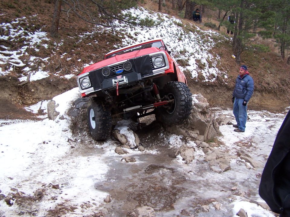Modified red off-road vehicle with large tires navigating rocky terrain in snow
