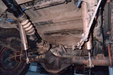 1990 Ford Bronco - Undercarriage view of a four-wheel-drive vehicle showing the front axle, driveshaft, shocks and steering tie rods.