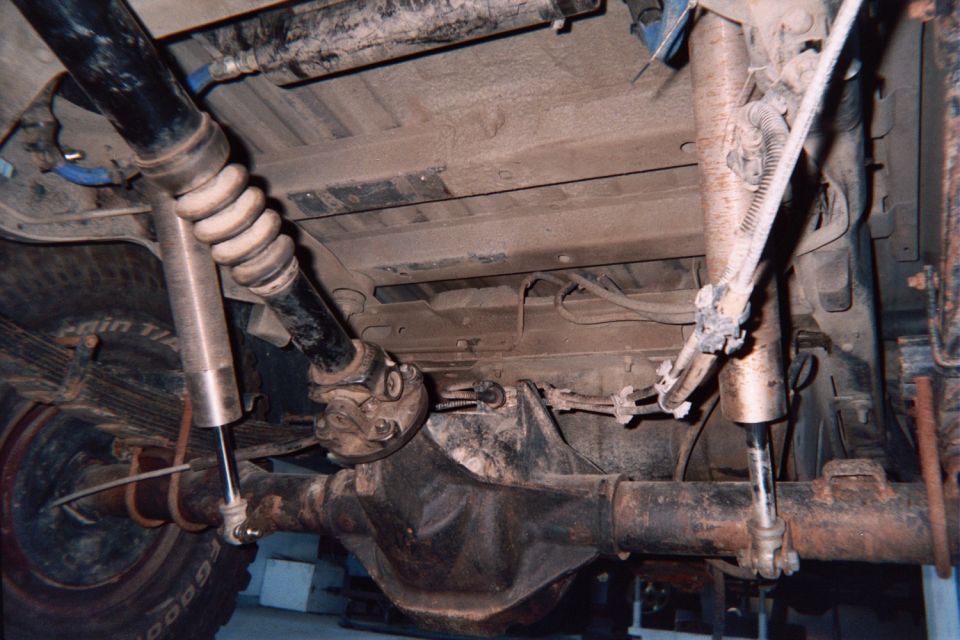 Underside of a 4x4 showing front axle, driveshaft, shock absorbers and steering linkage