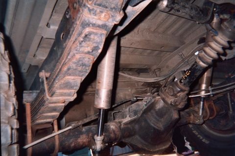 1990 Ford Bronco - Underbody view of a vehicle's rear suspension with leaf spring, shock absorber, differential and driveshaft visible.