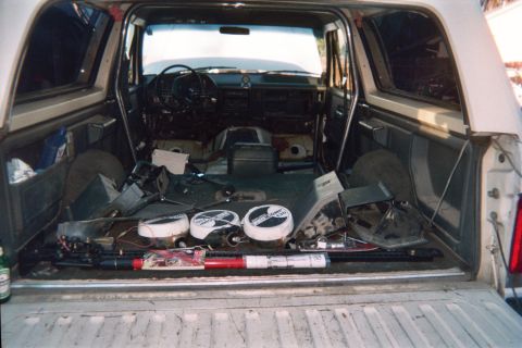 1990 Ford Bronco - View through the rear of a stripped SUV showing the bare cabin floor, dashboard and steering wheel with parts laid out.