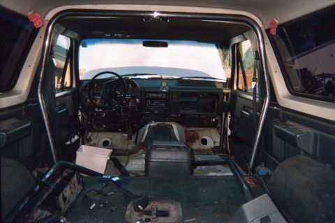 1990 Ford Bronco - Stripped SUV interior looking toward the dash and steering wheel with the floor exposed and a roll bar overhead.