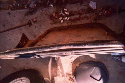 1990 Ford Bronco - rusty removed body panel with chrome trim lies on the dirt outdoors beside a shovel and two round bucket lids.