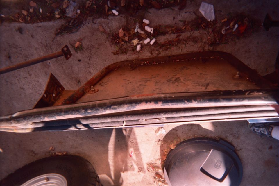 Removed automotive panel or bumper lying on dirt ground next to a shovel and bucket lids