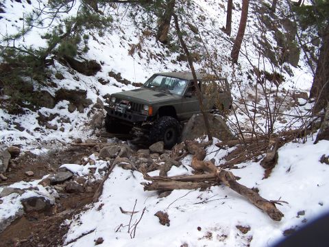 1985 Ford Bronco - A green Jeep Cherokee tackles a challenging off-road course covered in snow and rocks.