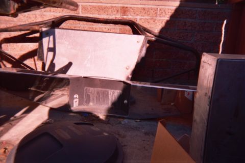 1990 Ford Bronco - Fabricated roll-cage tubing and a sheet-metal bracket lean against a brick wall outside in bright sunlight.