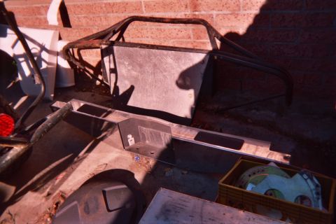 1990 Ford Bronco - tubular roll-cage frame and assorted metal fabrication parts are staged against a brick wall on the ground.