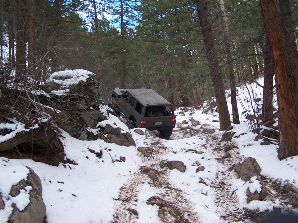Olive green SUV navigating a snowy, rocky trail in a forest