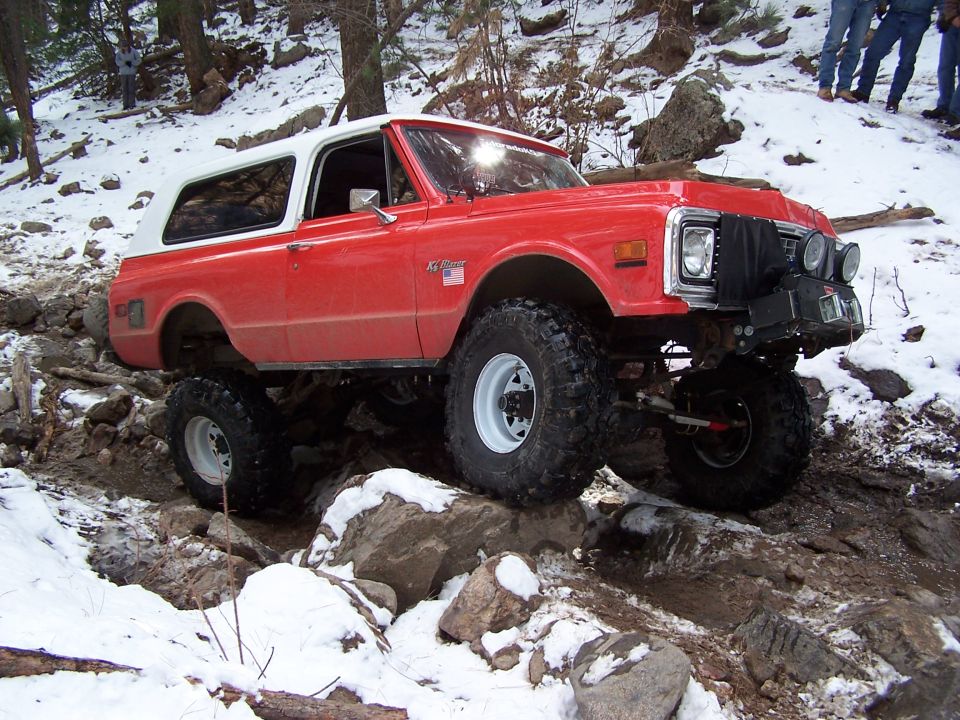 Red and white off-road SUV with large tires navigating rocky terrain in the snow