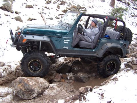 1985 Ford Bronco - A Jeep Wrangler navigates a rocky, muddy trail in a snowy environment.