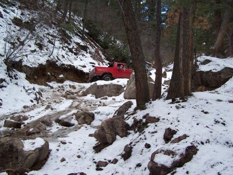 1985 Ford Bronco - Red pickup truck driving through a snowy, rocky terrain.