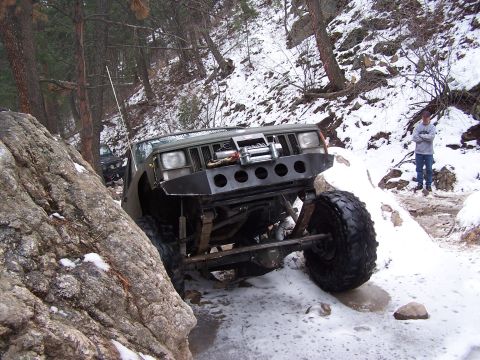 1985 Ford Bronco - An off-road SUV navigates a challenging rocky and snowy path, with another vehicle visible in the background.