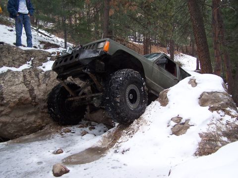 1985 Ford Bronco - This heavily modified Jeep Cherokee XJ is tackling a challenging off-road course in snowy conditions.