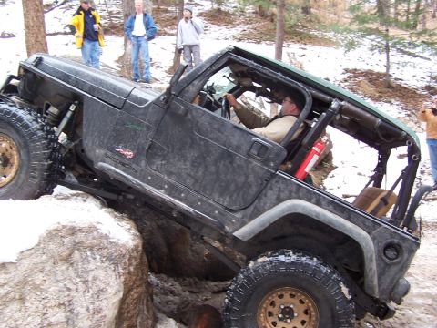 1985 Ford Bronco - A driver maneuvers a Jeep Wrangler over challenging rocky terrain, with onlookers observing the off-road adventure.