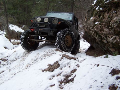1985 Ford Bronco - A heavily modified Jeep Wrangler navigates a challenging snowy and rocky terrain, its off-road capabilities.