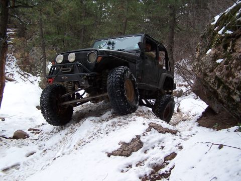 1985 Ford Bronco - A black Jeep Wrangler navigates a challenging snowy and rocky terrain.