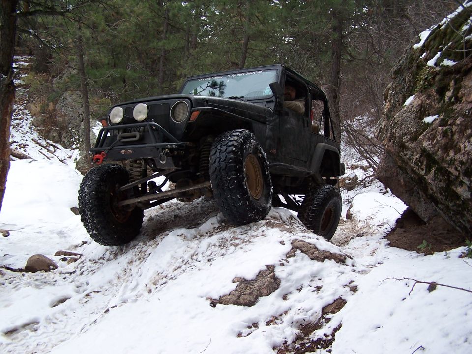 Black Jeep Wrangler off-roading on a snowy, rocky trail