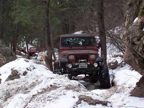 1985 Ford Bronco - Two Jeep Wranglers navigate a snow-covered, wooded trail in a mountainous area.
