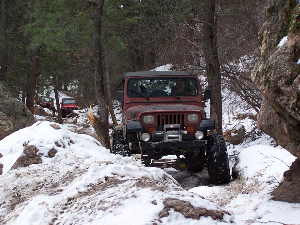 Maroon Jeep Wrangler on a snowy, rocky trail, front view with winch