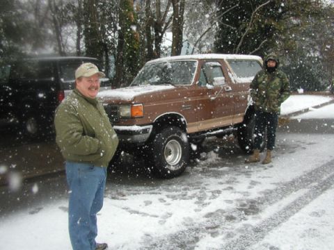 1988 Ford Bronco - Two men stand next to a lifted Ford Bronco in a snowy environment, with another vehicle partially visible.
