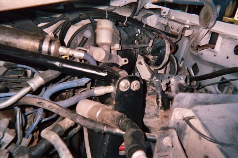 1990 Ford Bronco - Dense engine-bay view with tangled hoses, wiring, a fluid reservoir and brake components packed under the hood.