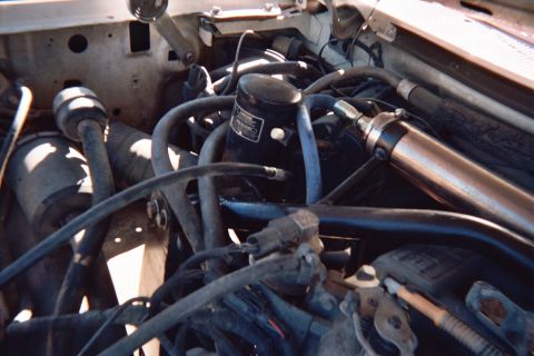 1990 Ford Bronco - Engine-compartment detail showing an ignition coil, routed vacuum hoses and a polished cylindrical component.