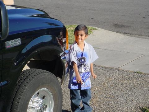 1999 Ford F-250 - A young boy stands beside a black 1999 Ford F-250 truck, showing the front fender and tire.