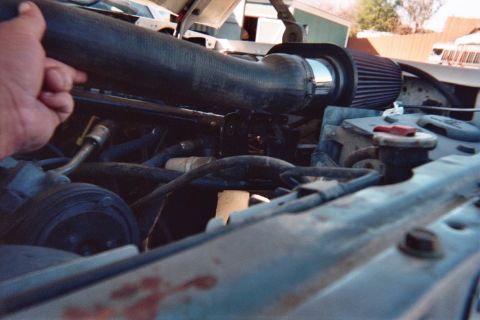 1990 Ford Bronco - hand holds a thick black radiator hose over an engine bay where a cone-style air filter is installed outdoors.