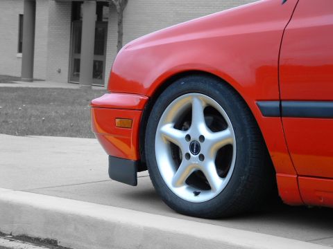 1994 Volkswagen Jetta - A red car is parked on a street, showing its front wheel and fender detail.