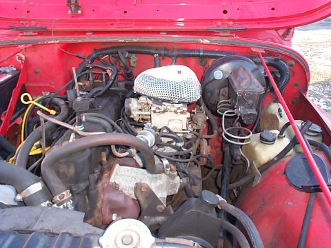 1989 Jeep YJ - Engine bay of a red 1989 Jeep YJ, the carburetor and air filter assembly.