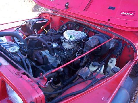 1989 Jeep YJ - Engine bay of a red 1989 Jeep YJ, an Edelbrock sticker on the inner fender.