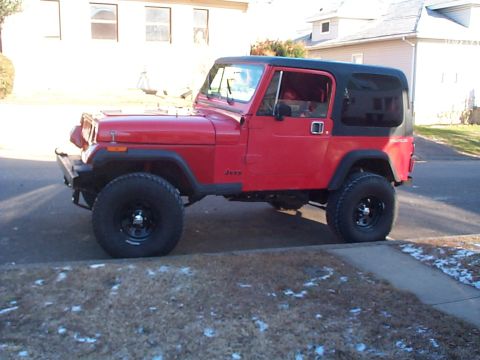 1989 Jeep YJ - A red Jeep CJ with a black soft top is parked on a residential street.